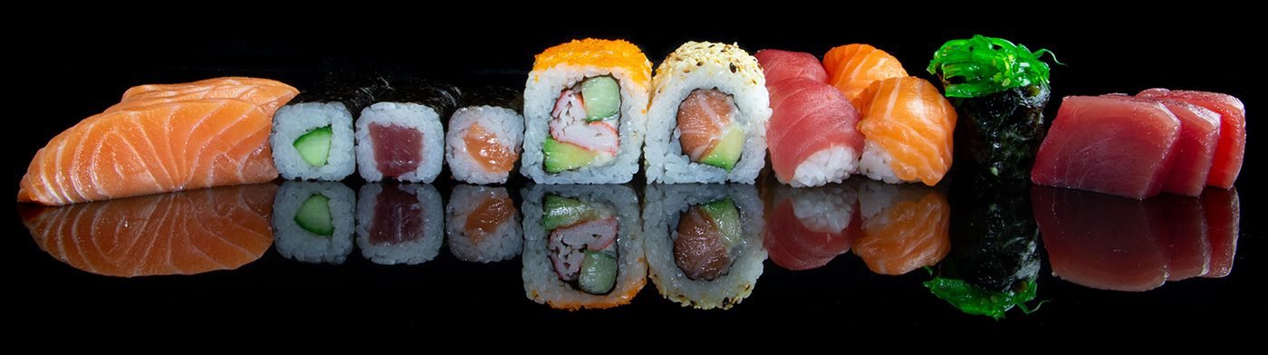 Een rij nigiri, maki en sashimi met zalm, tonijn en wakame op een zwarte, spiegelende ondergrond.